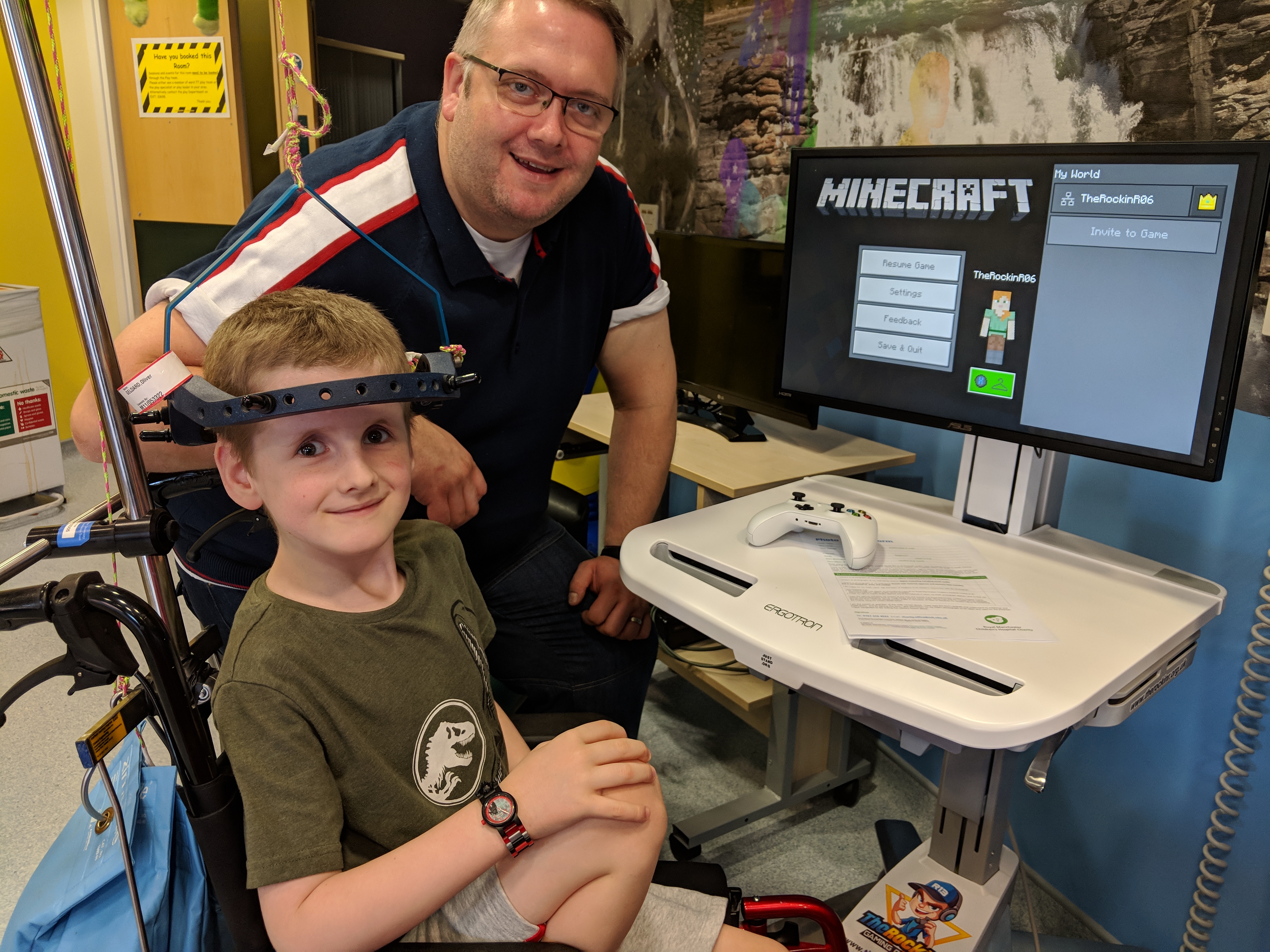 A boy playing Minecraft on an Xbox cart in his hospital room, with a GameChanger volunteer.